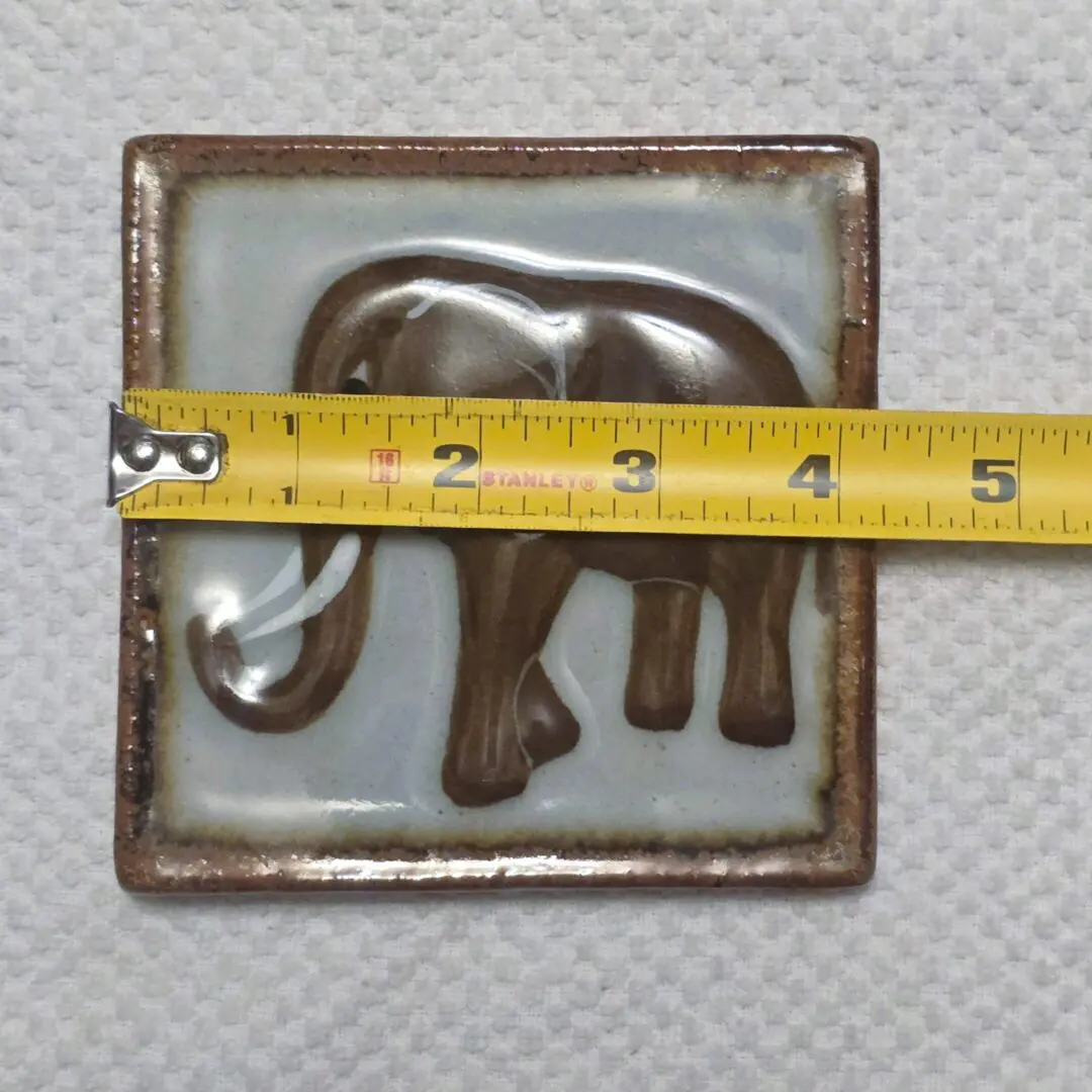A metallic elephant tile with a measuring tape across it.