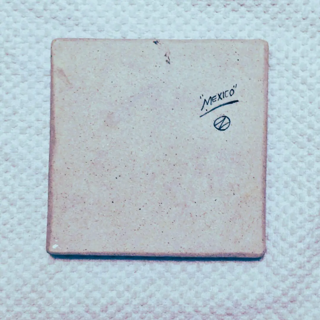 Square vintage tile with faded markings on a textured surface.