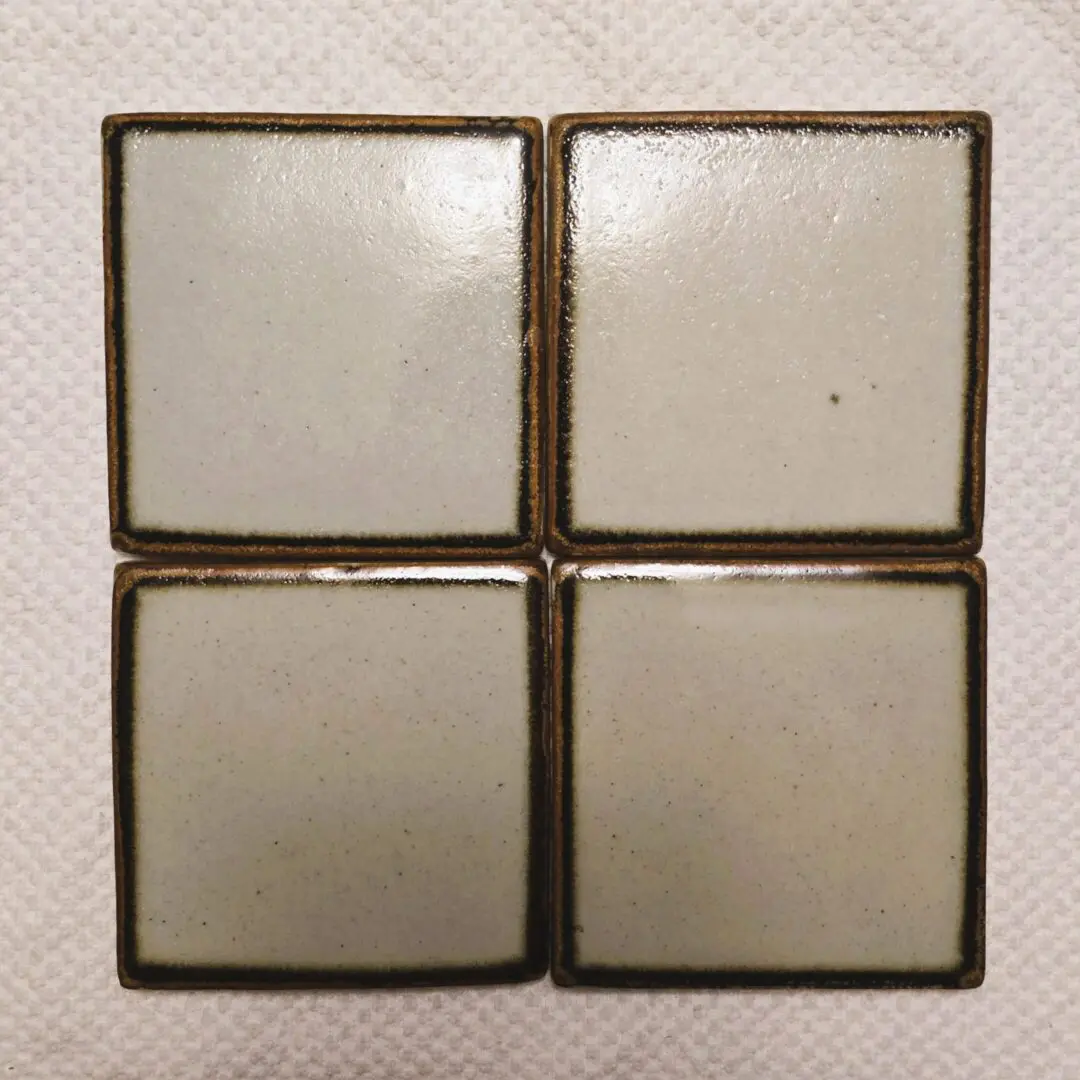 Four square white tiles arranged in a 2x2 pattern on a textured surface.
