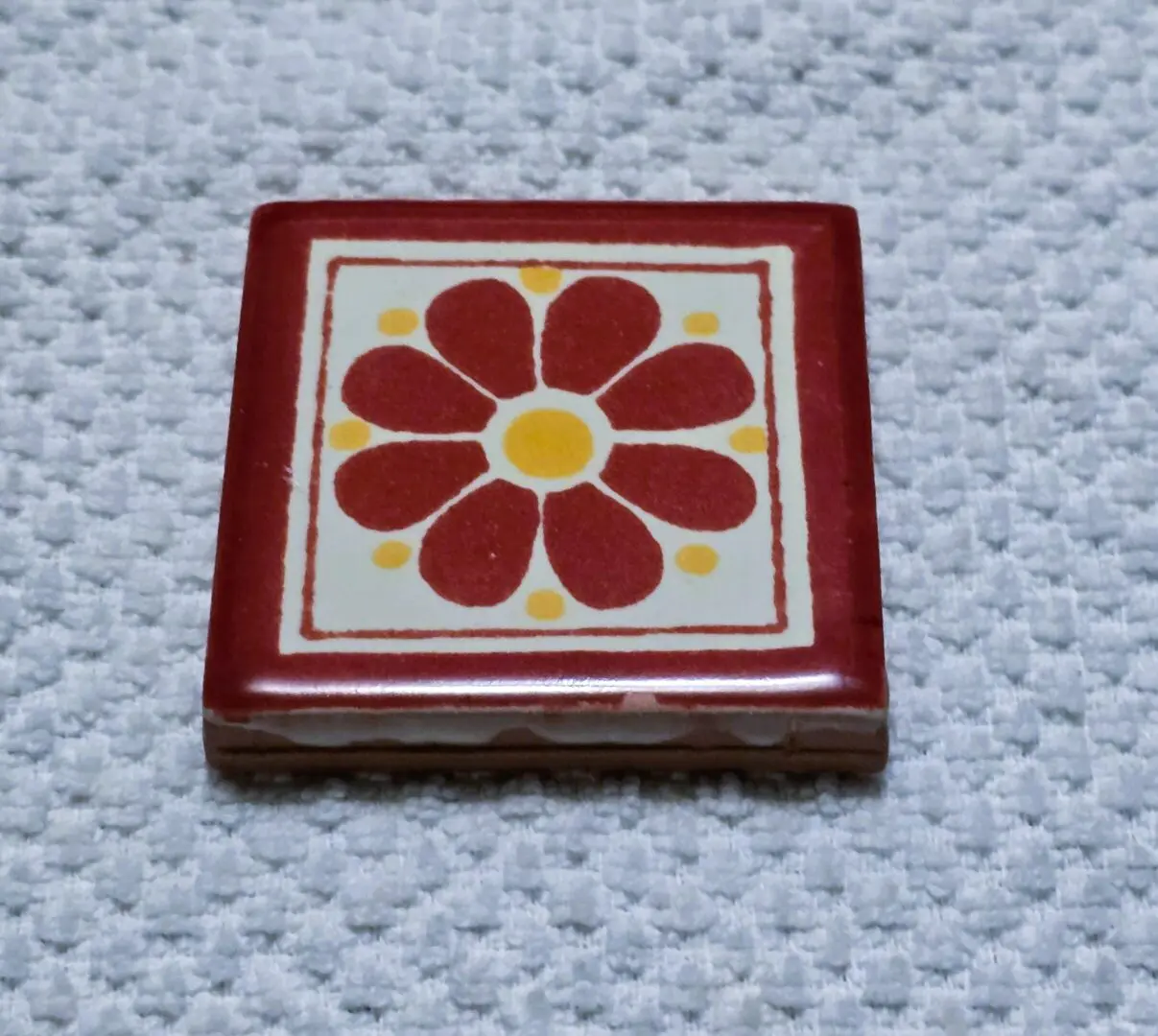 Red floral ceramic tile on textured surface.