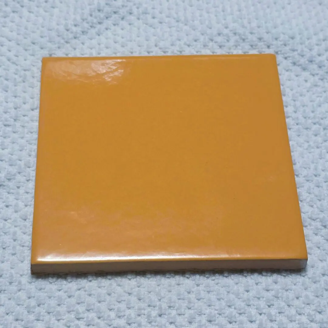 A square orange ceramic tile with a glossy finish.