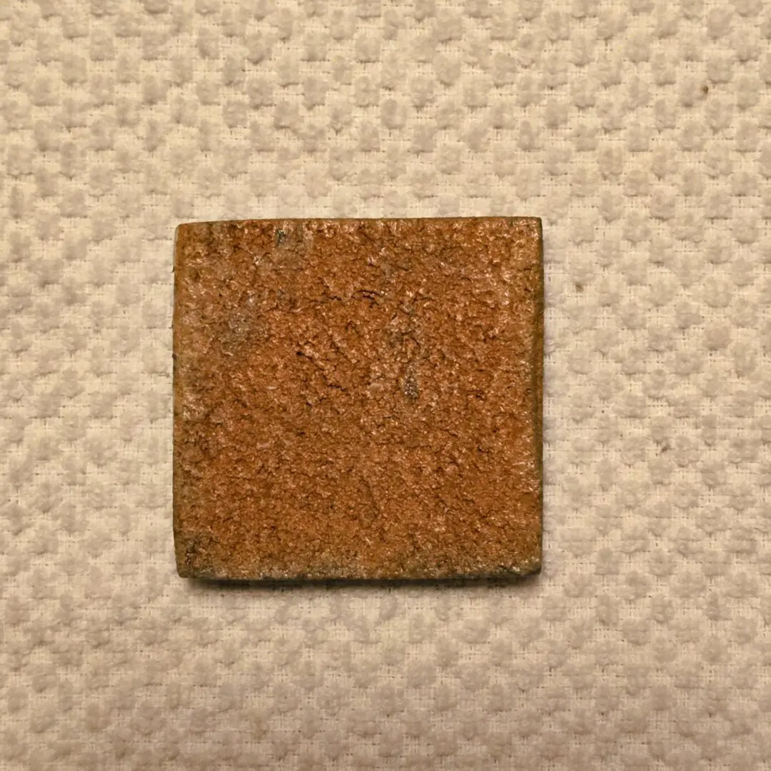 Square, textured tile on patterned surface.