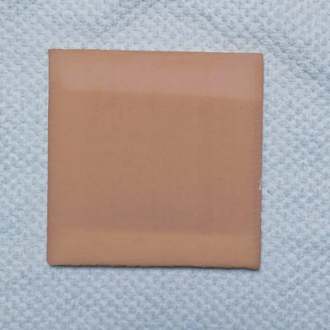 A square, light brown adhesive bandage on a textured white surface.