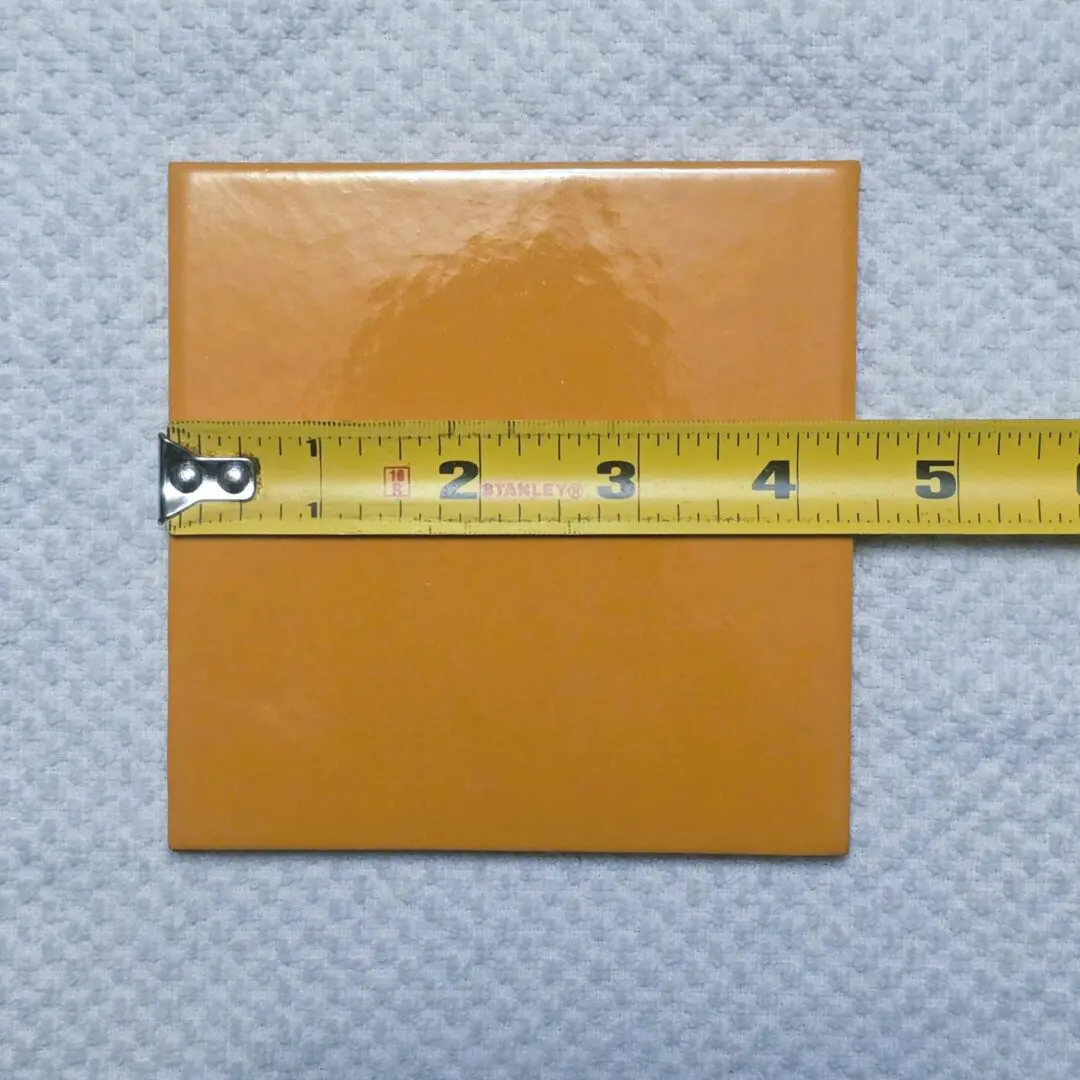 A yellow-orange square tile measured with a tape measure.