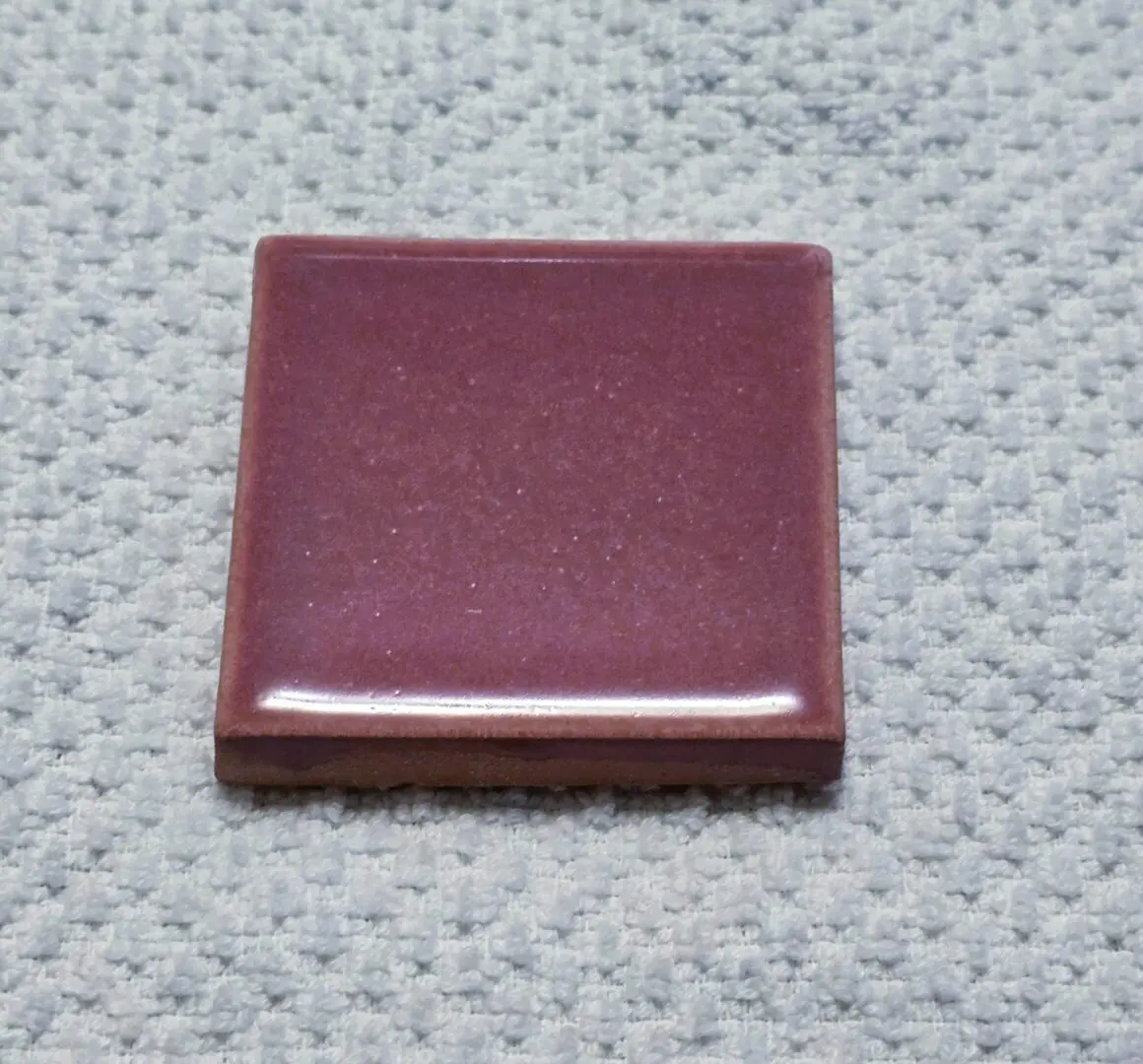 Glossy burgundy ceramic tile sample on fabric