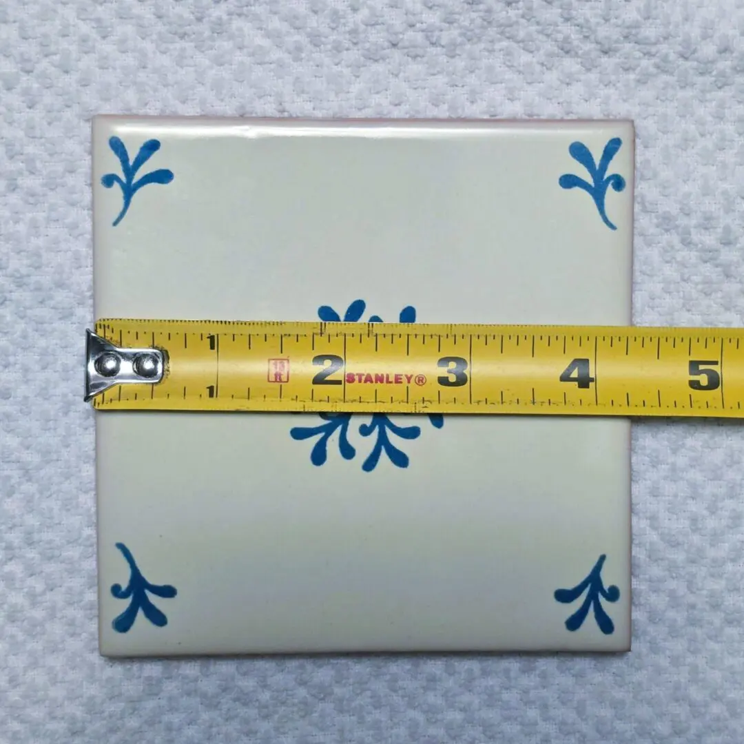 Tile with measuring tape on white surface.