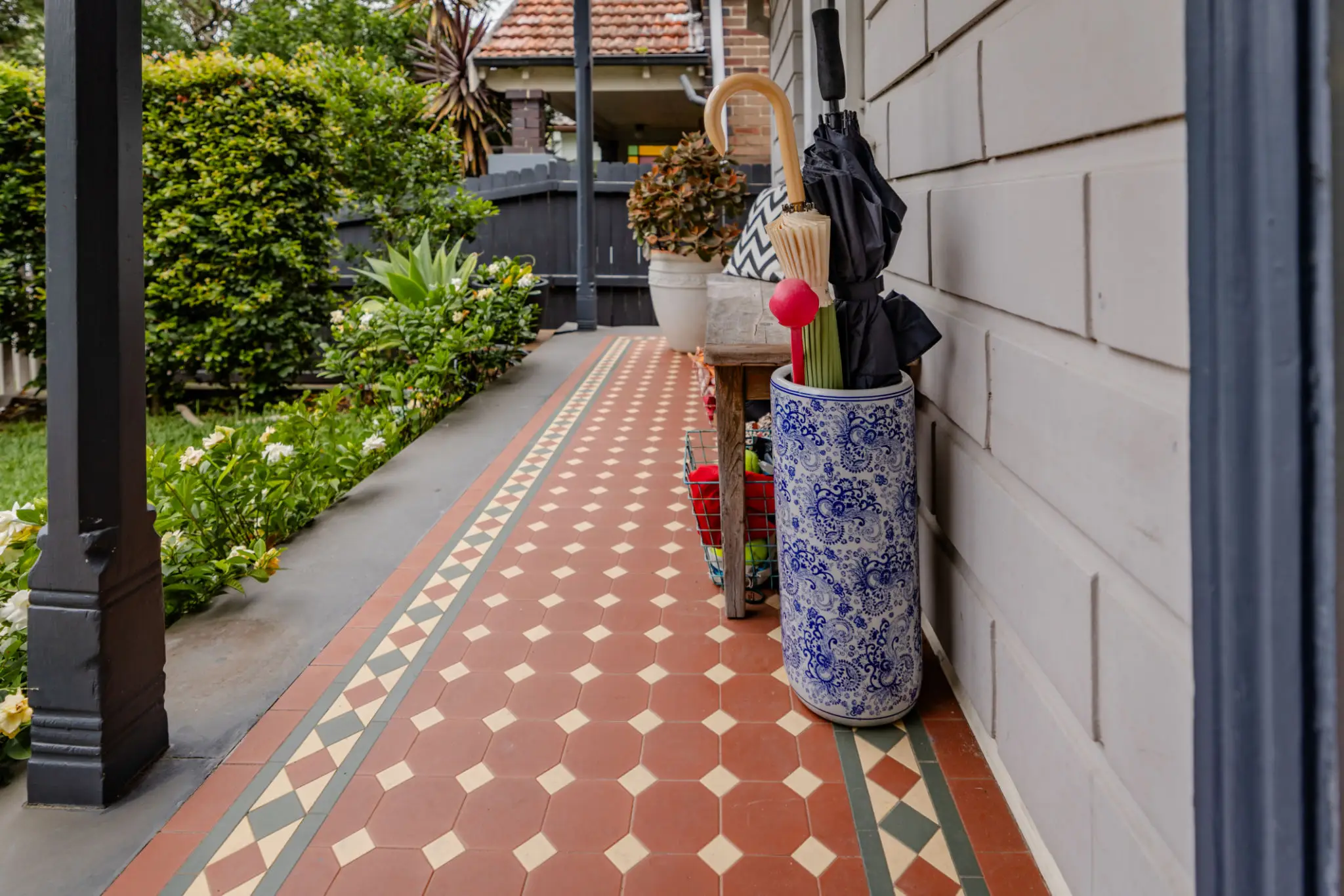 Decorative umbrella stand with umbrellas on a patterned tiled porch.